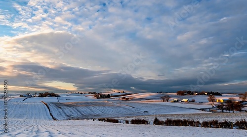 Snow-covered rolling hills under a dramatic twilight sky, with distant farmhouses glowing softly in the winter calm.