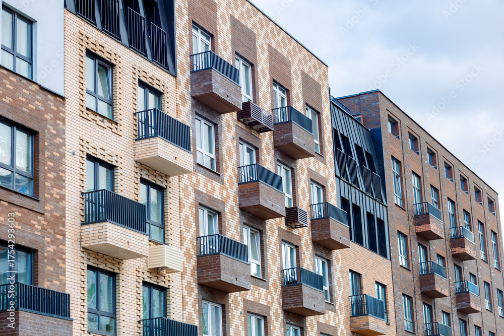 Obraz premium A modern residential complex with exposed brickwork, balconies, and large windows. The façade is finished in warm tones, with an emphasis on geometric shapes and stylish black railings.