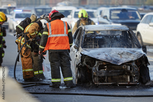 Bild auf Leinwand Group of firefighters and emergency responders extinguishing burning car on city
