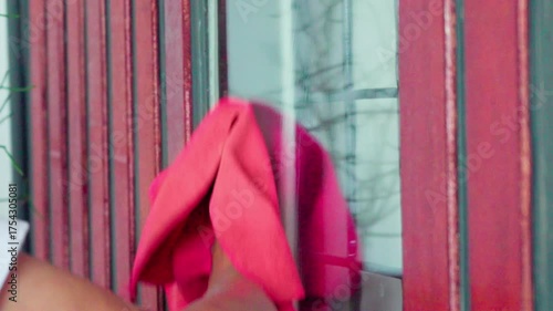 Close-up of a person cleaning a window with a red chamois cloth, showing home maintenance, household chores, and hygiene practices. Ideal for use in lifestyle blogs and cleaning service promotions