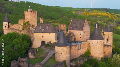 bourscheid castle château de green valley cover hills behind walls towers exterior structure visitor parking windmill atop to left right up close circling drone 