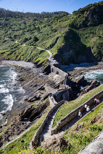 Discover the breathtaking beauty of San Juan de Gaztelugatxe, as tourists explore the iconic stone bridge and winding steps on the Basque coast, Spain