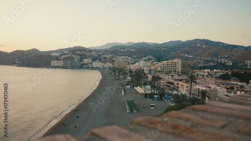 Wallpaper Mural High wide shot showing a quiet beachfront lined with palm trees and buildings, backed by rolling hills—soft golden light adds calm and depth. Torontodigital.ca