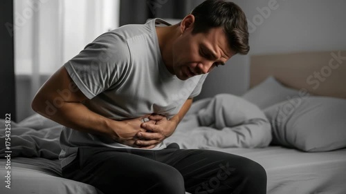 Man experiencing abdominal pain while sitting on the edge of his bed