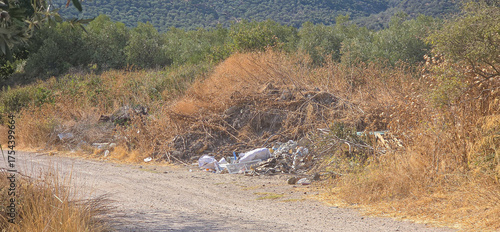 A rural dirt road with scattered trash and dry vegetation.