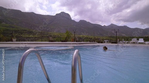 Woman Swimming in Infinity Pool with Scenic Mountain View on Cloudy Day