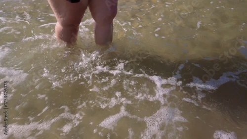Women's legs standing in the sea and creating splashes, holidaying on the coast, side view