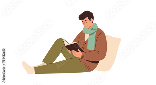 Man reading a book while sitting on the floor with a pillow behind him.
