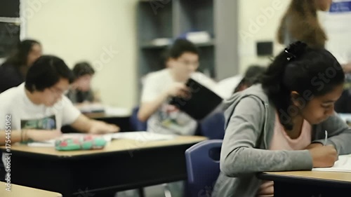 Classroom scene; student writing at desk, peers blurred in the background