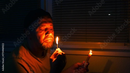Blackout, No electricity. Man in a dark room near a window with candle. Depressed young man during a power outage.