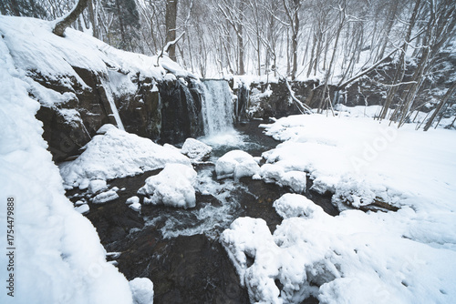 Frozen waterfall cascading through a snow-covered valley, representing the peaceful beauty and stillness of winter nature in Japan.