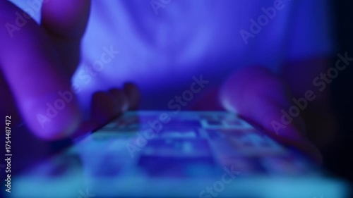 Close up of hands using a mobile phone in low light, browsing social networks and consuming endless online content. Doomscrolling and information overload.