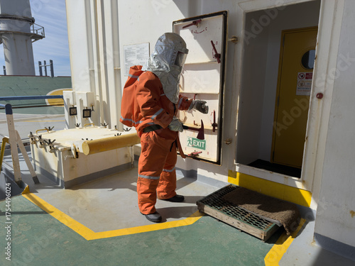 A sailor in full firefighting gear with a fire axe stands on the ship’s deck, preparing to enter the superstructure for inspection and fire suppression. Crew fire drill on a maritime vessel