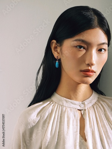 Close-up of a young Asian woman in a soft blouse with earrings showcasing modern beauty.
