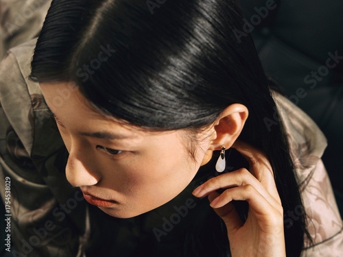 Woman in elegant attire with statement earrings adjusting her hair, conveying modern elegance and confidence.