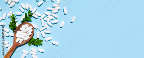 White tablets, vitamins, pills and green leaf in wooden spoon on blue background top view. Medical pharmaceutical background, health concept, organic dietary supplements, self care