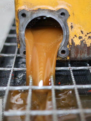 High-viscosity, brown fluid being drained from the circular opening of a transmission, flowing over a metal grate in a service bay.