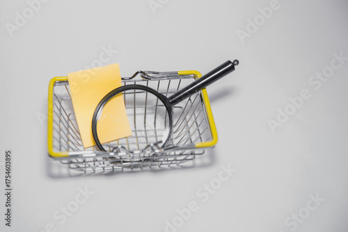Secret shopper or mystery shopper concept with a magnifying glass and a shopping basket or trolley isolated on a white background and copy space
