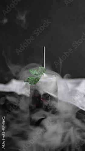 Smoky dark drink with mint in a glass, effervescing amidst swirling white vapor against a deep background