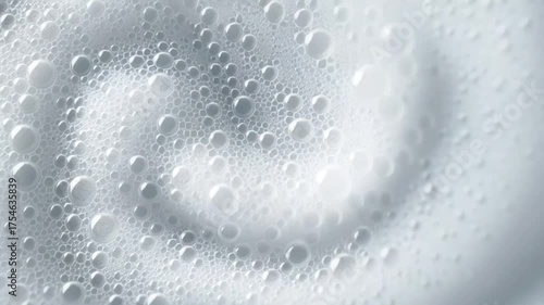 White soap foam rotates forming spiral pattern with bubbles spreading outward creating dynamic circular motion in cleaning hygiene concept with light blue background