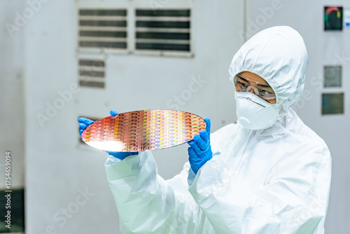 Fotografija A female worker in protective clothing inspects silicon wafers at a semiconducto