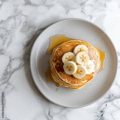 A stack of pancakes with bananas on top. The plate is white and the bananas are yellow. The pancakes are fluffy and the bananas are sliced