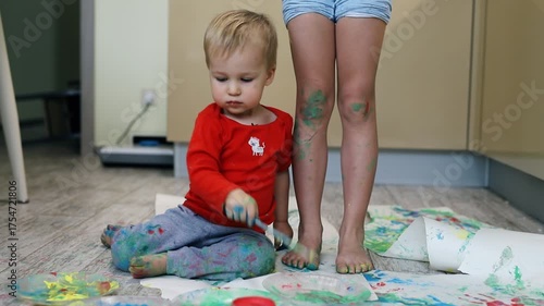 Adorable cute caucasian little blond siblings children enjoy having fun together with mother painting brush and palm at home indoors . Cheerful happy kids smiling drawing masterpiece art picture