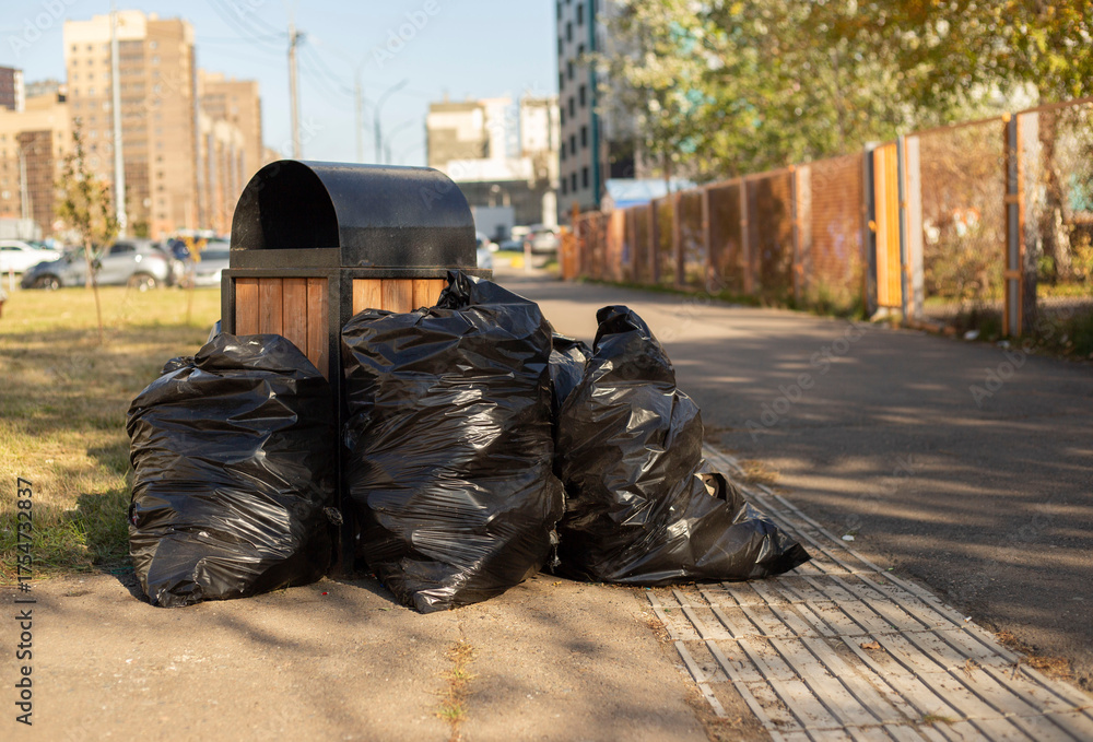 Obraz premium Trash can surrounded by a bunch of garbage bags on street. bags filled with trash on the street. dirty street concept, garbage collection, environmental pollution