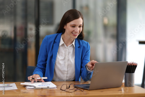Obraz na plátně Businesswoman taking notes while having video call on laptop in office