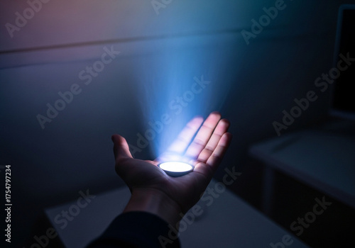 A hand holding a glowing object that emits a beam of light upwards.