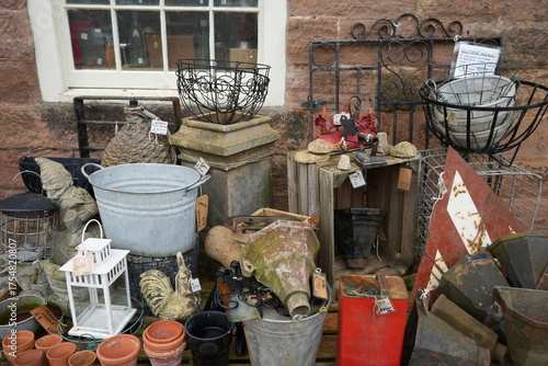 Assortment of vintage garden decor, antique tools, and metal planters for sale outside a stone building window at Cromford Mills, Derbyshire, England.