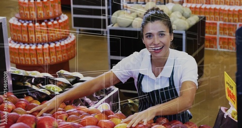 Organizing clerk in green-striped apron leaning over red apples at market produce, with juice trays