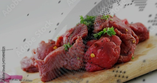 Lying raw beef chunks on wooden cutting board in kitchen with parsley, cracked pepper, onion slices