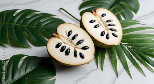 Ripe custard apple fruit halved revealing black seeds and lush green tropical leaves