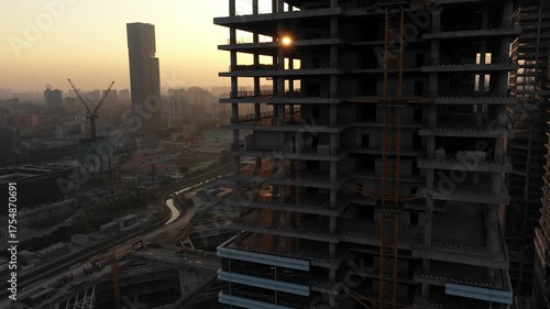 Rising drone shot of tower under construction, with the sun flaring between the building's floors, urban development in Guangzhou, one of China's largest cities