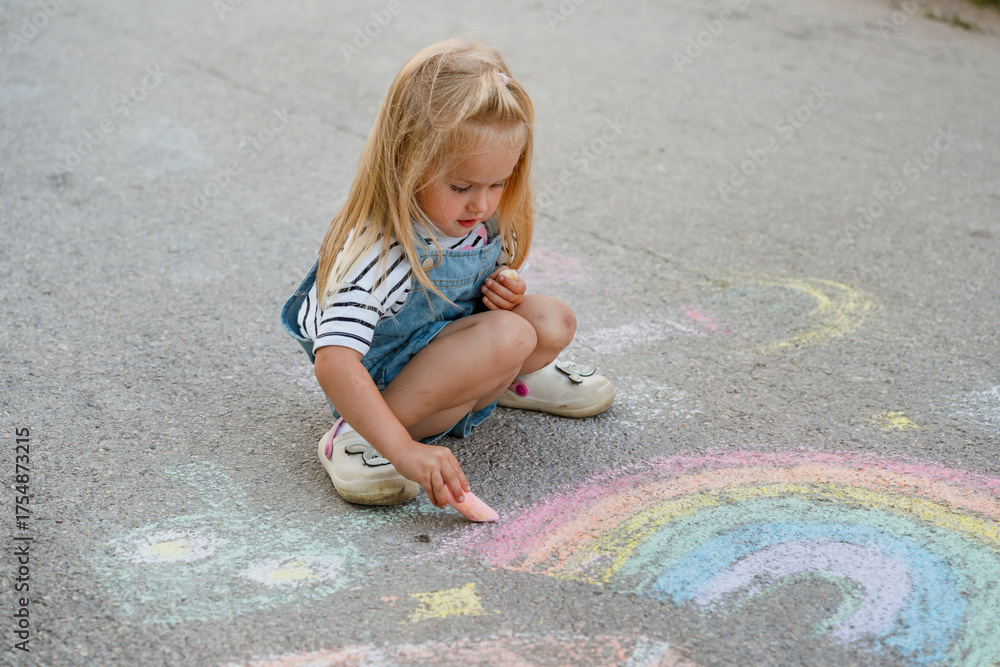 Fototapeta premium Cute little girl draws with crayons on asphalt.