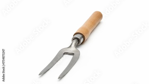A metal carving fork with a wooden handle lies diagonally against a white backdrop, angled toward the viewer. The fork's tines are sharp