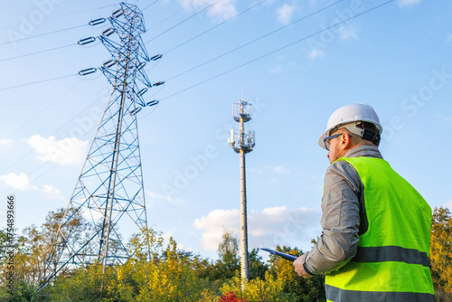 Male engineer maintains a telecommunications tower and power lines. Inspecting 4G and 5G network equipment. Control and maintenance of electrical installations for cellular communications.