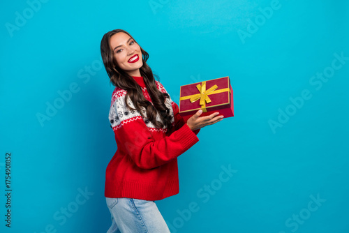 Papier peint Cheerful woman in festive sweater holding gift box against blue wall, celebratin