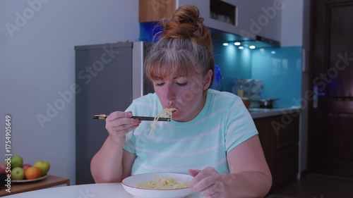 A millennial woman eats Asian noodles with chopsticks. A woman eats street food at home