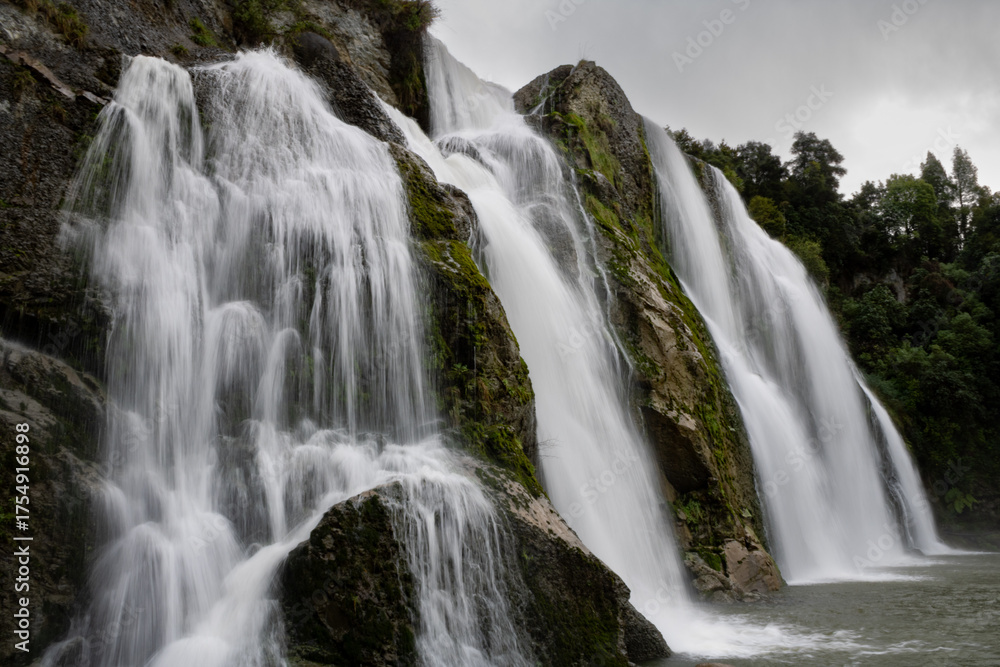 Obraz premium Giant cascading waterfall over green moss covered rocks in New Zealand 