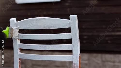 Man with paint brush painting old wooden chair in white color