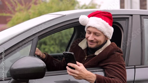 Online Shopping Application. Happy Man in Christmas Santa Hat Using Phone Sitting In Car, Searching Best Christmas Gift Via Marketplace App.