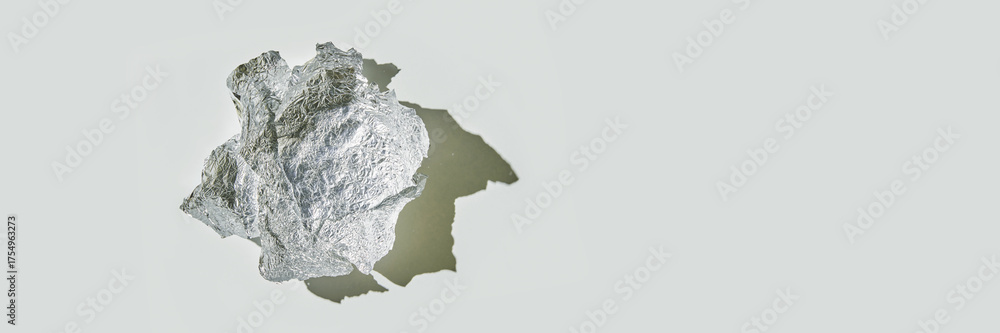 Fototapeta premium Crumpled aluminum foil ball casting shadow on light gray surface.