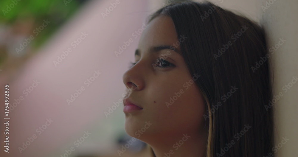 Naklejka premium Young girl leaning against a wall, close-up profile showing calm and reflective expression, symbolizing peace, youth, and mindfulness in an everyday setting