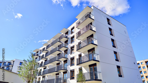 A residential building  by lush green trees and surrounded by  fresh vegetation on a clear sunny day. Modern architecture residential apartment building complex surrounded by greenery.