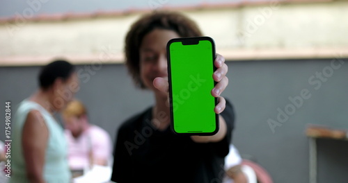 Wallpaper Mural Young boy holding smartphone with green screen chroma key, smiling outdoors in casual courtyard setting, people blurred in background Torontodigital.ca