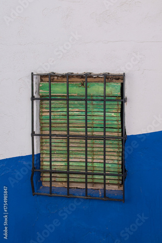 A typical blue and white wall in La Mancha with a window with a green grille and shutter in Campo de Criptana, Ciudad Real province, Spain.