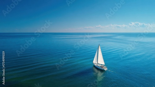 A sailboat moves smoothly across calm waters surrounded by endless blue skies and gentle waves.