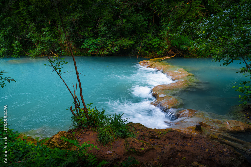 Obraz premium Turquoise river, rocky waterfall and greenery in summer forest